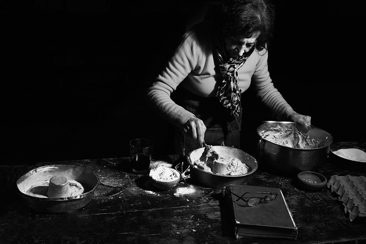 Blanca Lanzy en blanco y negro, de pie frente a una mesa de madera con fuentes, harina y un libro con anteojos encima