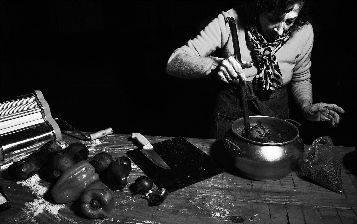 Blanca Lanzy en blanco y negro, junto a una olla, con morrones, cebollas y una máquina de pastas sobre la mesa