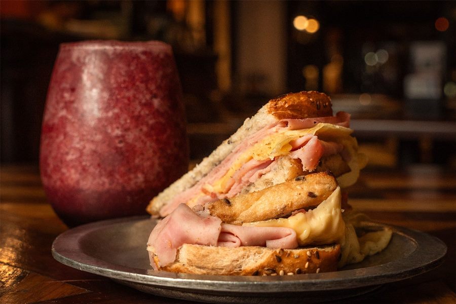 Tostadón clásico de jamón y queso en pan con semillas, con un licuado de fruta natural