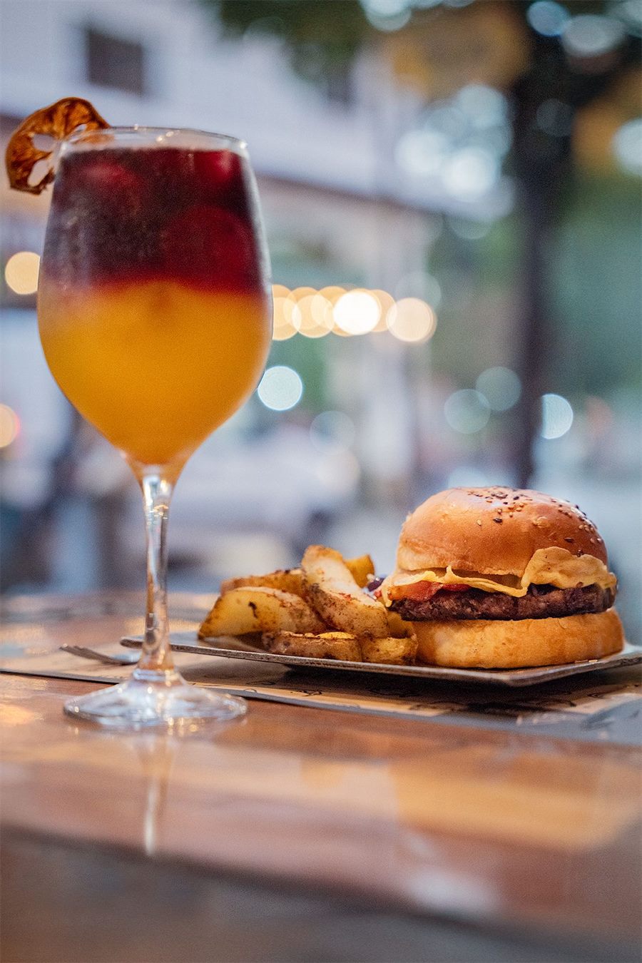 Un trago y una hamburguesa con papas en una mesa de la vereda, con la calle de fondo
